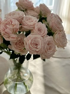 a glass vase filled with pink roses on top of a white tablecloth covered table