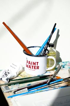 some paint brushes are sitting in a cup on a table next to other paints and pencils