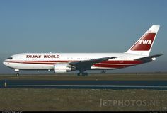 a red and white plane is on the runway in front of an airport sign that says trans world