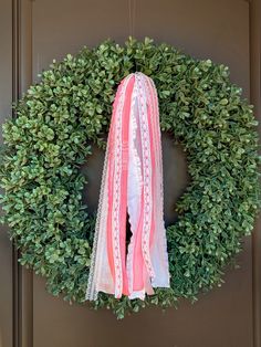 a wreath hanging on the front door with pink and white ribbons tied around it's edges