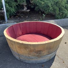 a wooden barrel sitting on top of a sidewalk next to bushes and shrubbery in the background