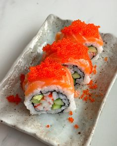 two sushi rolls on a white plate with red cauliflower sprinkles