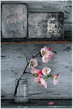 pink flowers are in a glass vase on a wooden table next to a brick wall