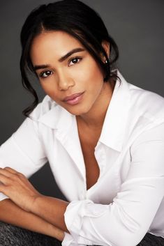 a woman in white shirt sitting down with her arms folded over her chest and looking at the camera