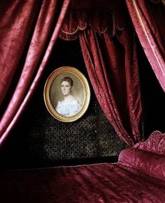 a bed with red curtains and a portrait on the headboard in front of it