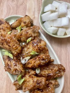 chicken wings with onions and scallions on a plate next to a bowl of ice cubes