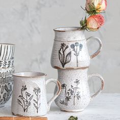 three mugs with designs on them sitting next to each other and one has a flower in it