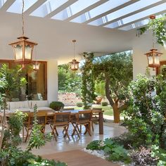 an outdoor dining area with lots of greenery and hanging lights over the table,