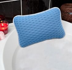 a blue pillow sitting on top of a white bath tub next to a red candle