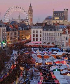 an aerial view of a christmas market with ferris wheel and buildings in the background at dusk