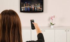 a woman holding a remote control in front of a flat screen tv on the wall