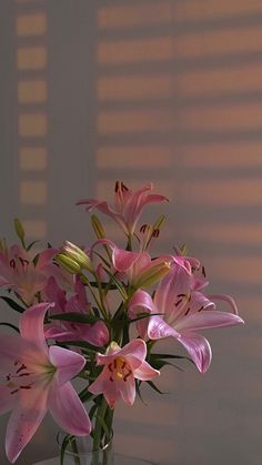 a vase filled with pink flowers sitting on top of a table next to a window