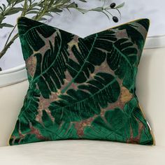 a green and gold pillow sitting on top of a white couch next to a potted plant