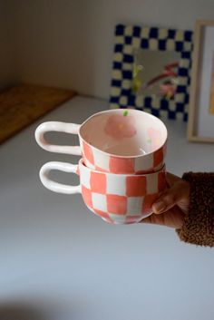 a person holding two coffee cups in their left hand, with one being held up by the other