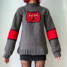 a woman with red hair is wearing a gray knitted sweater that has an image of a cat on it