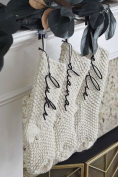 three knit stockings hanging from a mantel with greenery in the corner and on top