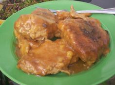 a green plate topped with meat covered in gravy next to a fork and potted plant