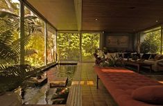 a living room filled with lots of windows next to a small pond and couches