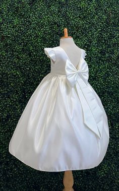 Our enchanting Ankle Length flower girl dresses are sure to turn heads! This beautiful elegant sophisticated dress is handmade, the bodice consists of Ivory Bridal Satin with a sowed in sash at the waist, the back of the dress consists of an open V-back with a hidden zipper. The big bow is detachable. The skirt consists of Ivory satin followed by lining and crinoline for a fuller look. Extremely light weight and beautiful. This dress is perfect for any occasion!  Dress Is Pictured with a pettico Elegant Spring Princess Dress For Baptism, Cream Princess Dress For First Communion, Elegant Spring Baptism Dress, Cream Wedding Dress With Bow, Elegant First Communion Dress For Spring, Elegant Princess Dress With Ruffles For First Communion, Elegant Spring First Communion Dress, Princess Dress With Satin Bow For Baptism, Fitted Cream Princess Dress For First Communion