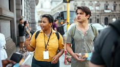 a man and woman walking down the street talking to each other while holding something in their hands