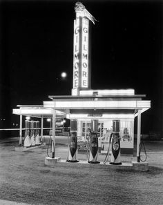 an old gas station at night with the neon sign lit up in black and white