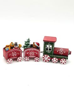 a red and green toy train with christmas decorations on it's sides, sitting in front of a white background