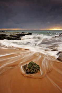 a rock sitting on top of a sandy beach next to the ocean under a cloudy sky