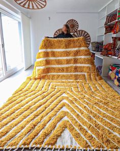 a large yellow blanket on top of a bed in a room filled with shelves and toys