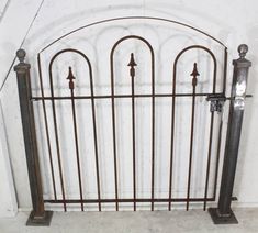 an old iron gate with four posts and two knobs on each side, in front of a white wall