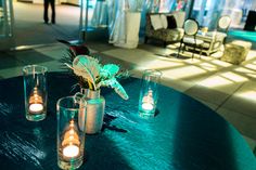 three vases filled with candles on top of a blue table cloth covered round table