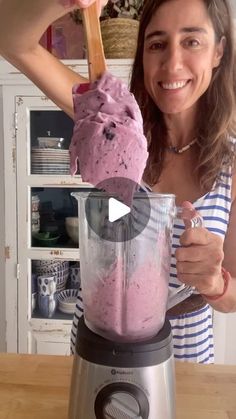 a woman is holding a spoon in a blender with pink ice cream on it