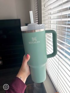 a person holding up a starbucks cup in front of a window with blinds on it