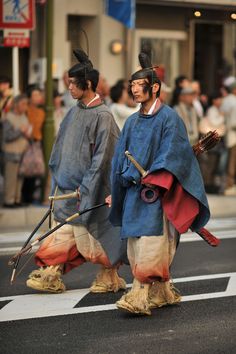 two men dressed in traditional japanese garb cross the street while people watch from behind