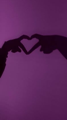 two hands making a heart shape with their fingers against a purple background that appears to be in the air