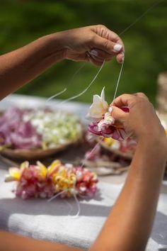 two hands are holding flowers and stringing them on a table with other dishes in the background