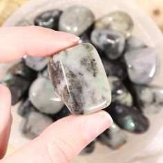 a person holding a rock in their hand with other rocks behind it on the table