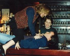 three people are sitting at a bar and one person is on the counter with his head down