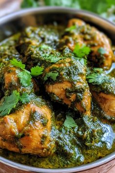 a bowl filled with chicken and spinach covered in pesto sauce on top of a wooden table