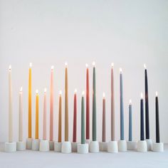 seven candles lined up in different colors and sizes with one candle lit on each side