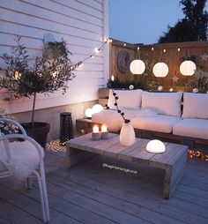 an outdoor living area with white furniture and string lights on the roof terrace at night