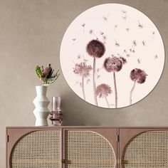 a white vase with flowers on it next to a brown cabinet and wall mounted artwork