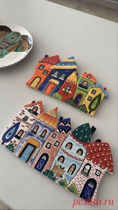 three ceramic houses sitting on top of a white table next to a plate with a decorative design