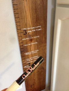 a person holding a pen in front of a wooden ruler with writing on the side