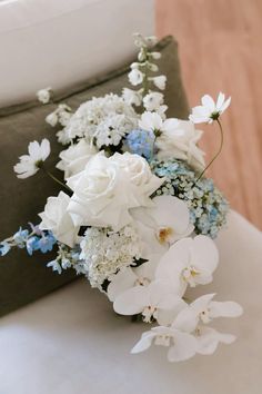 a bouquet of white and blue flowers sitting on top of a couch next to a pillow