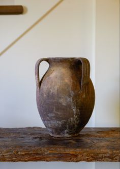 an old brown vase sitting on top of a wooden table next to a white wall