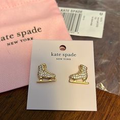 a pair of gold toned earrings with white crystals on them sitting next to a pink bag