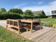 a wooden table and chairs sitting on a deck near a pond in the middle of a yard