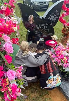 two women are sitting in front of a memorial with pink flowers and a black butterfly