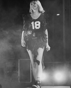 a woman in a football uniform is standing on stage with her legs spread out and lights shining behind her