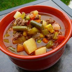 a red bowl filled with meat and vegetables on top of a table next to a window